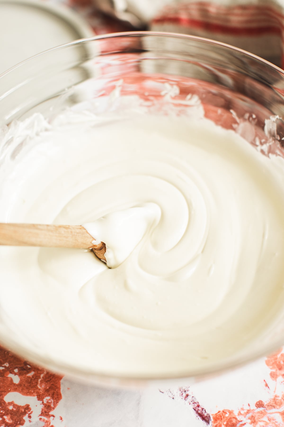 Melted white chocolate in a bowl with a wooden spoon for making Christmas Chex Mix.