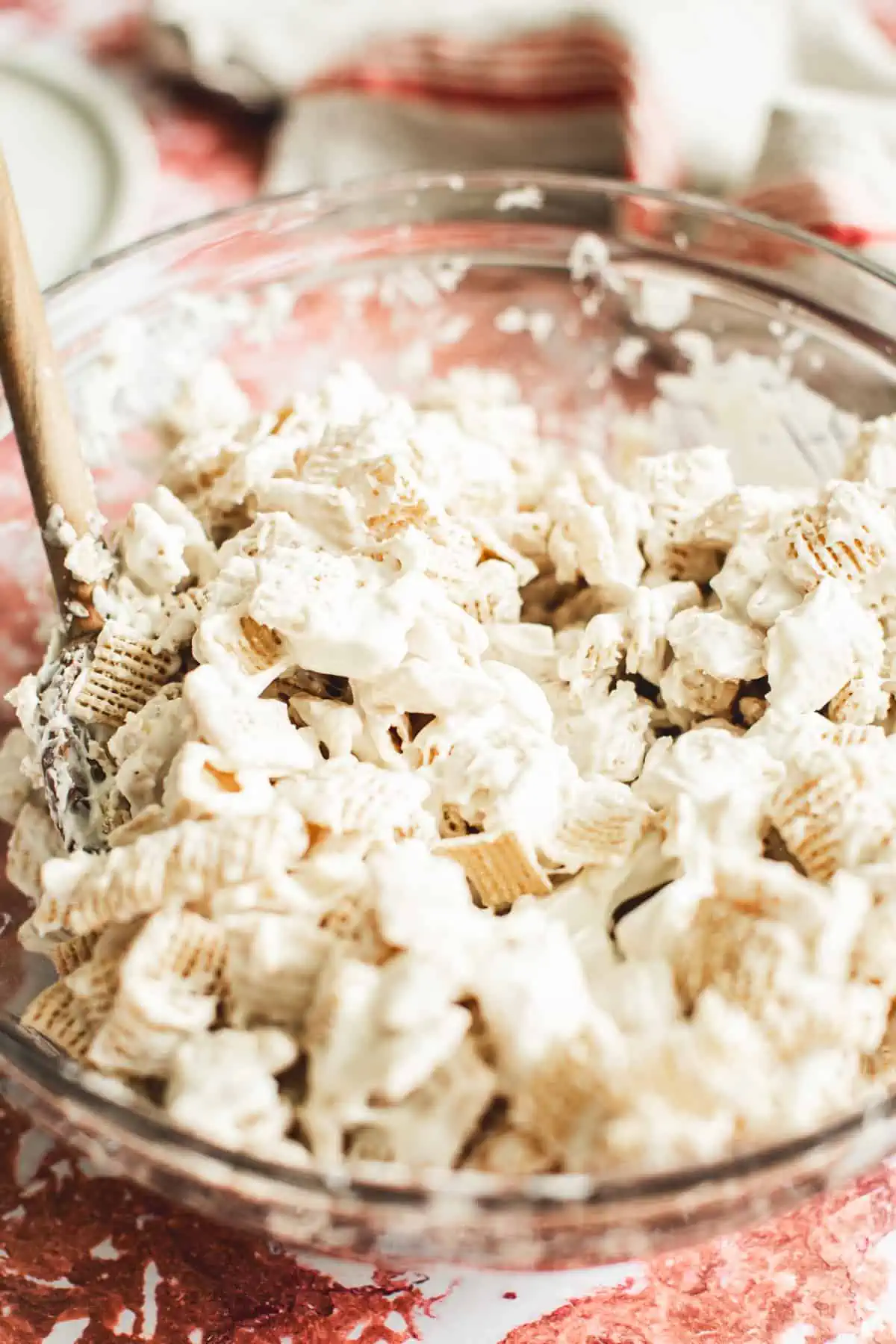 Chex cereal mixed with melted white chocolate in a mixing bowl for making Christmas Chex Mix.