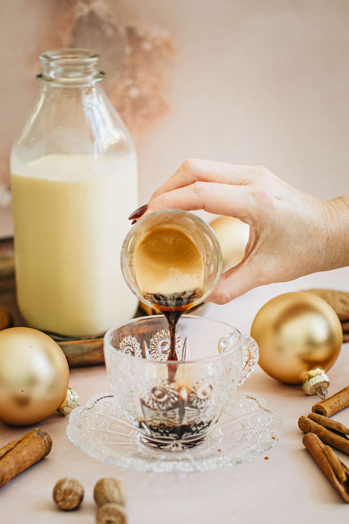 Pouring a shot glass filled with espresso into a glass coffee cup on a saucer for making an eggnog latte.