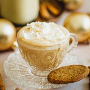 Eggnog Latte in a glass cup with a saucer. The latte is topped with whipped cream and nutmeg.