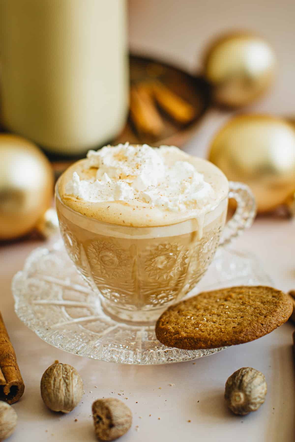 Eggnog Latte in a glass cup with a saucer. The latte is topped with whipped cream and nutmeg.