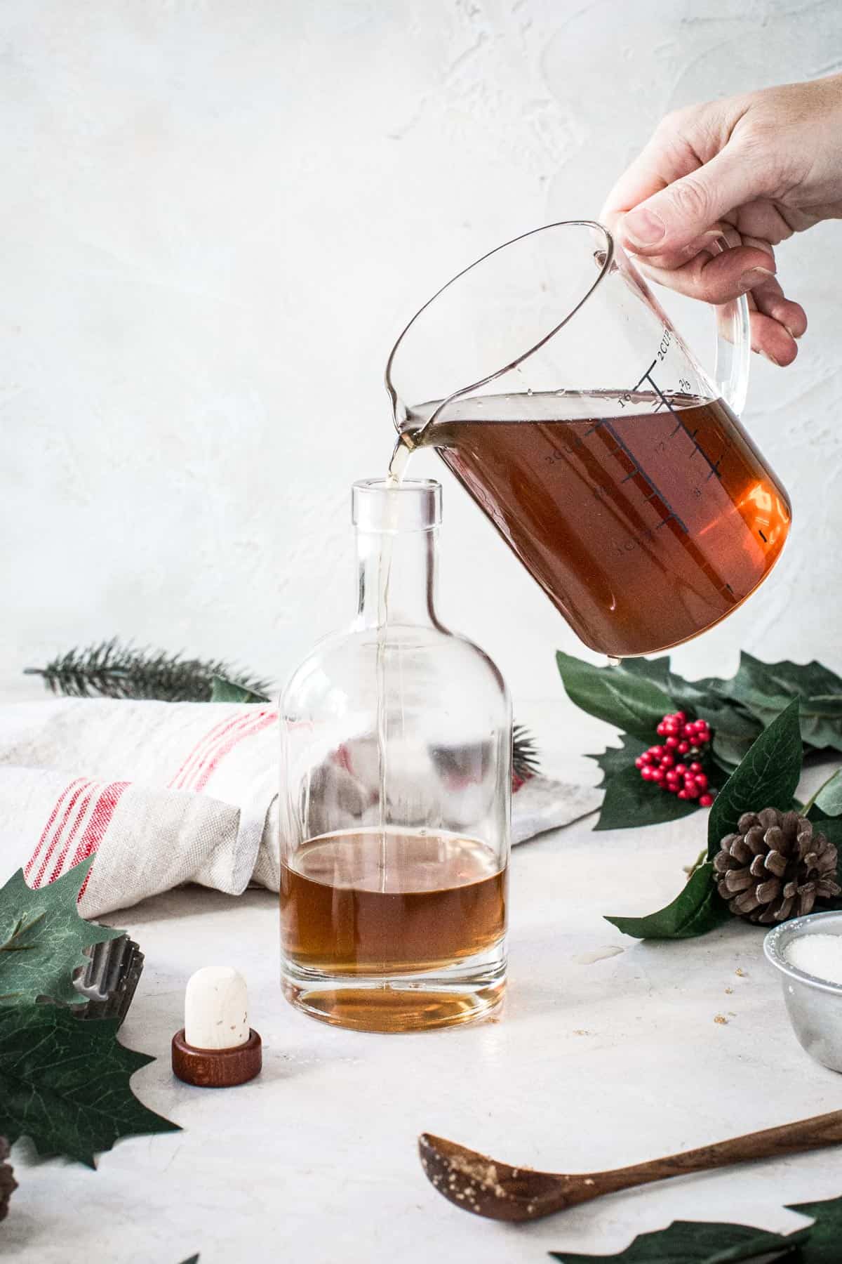 Measuring cup filled with homemade amaretto liqueur pouring it into a bottle.