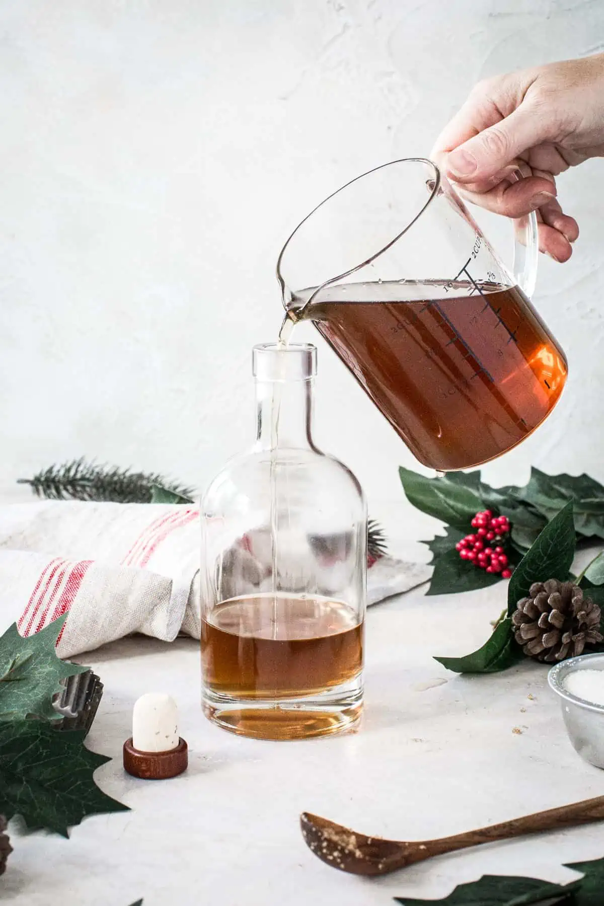 Measuring cup filled with homemade amaretto liqueur pouring it into a bottle.