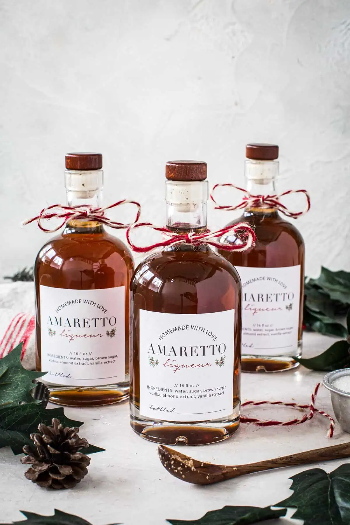 Three bottles of homemade amaretto with homemade labels and bakers twine around the neck.