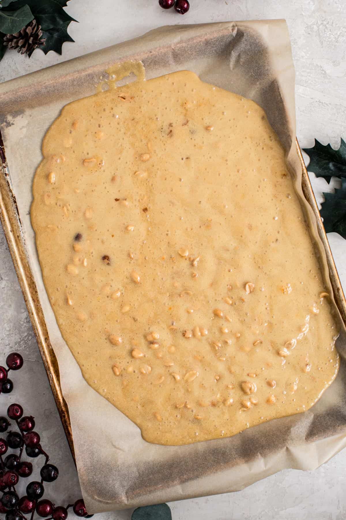 Peanut brittle spread onto a parchment-lined baking sheet.