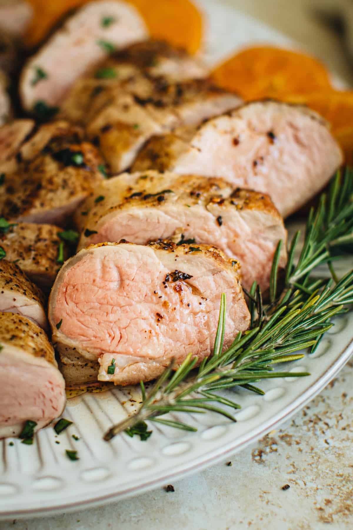 Sliced sous vide pork tenderloin on a serving plate with fresh rosemary for garnish.