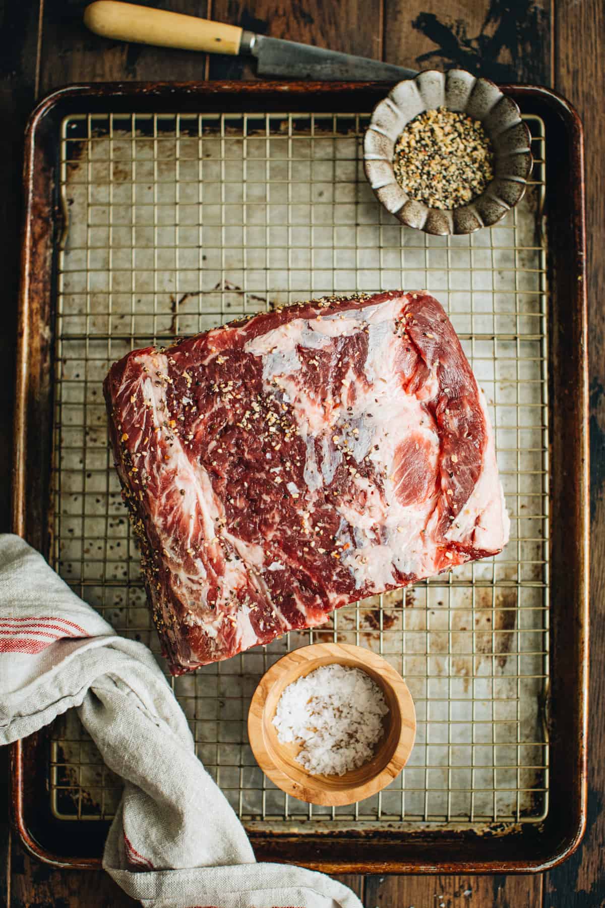 Salted rib roast sitting on a wire rack over a baking sheet.