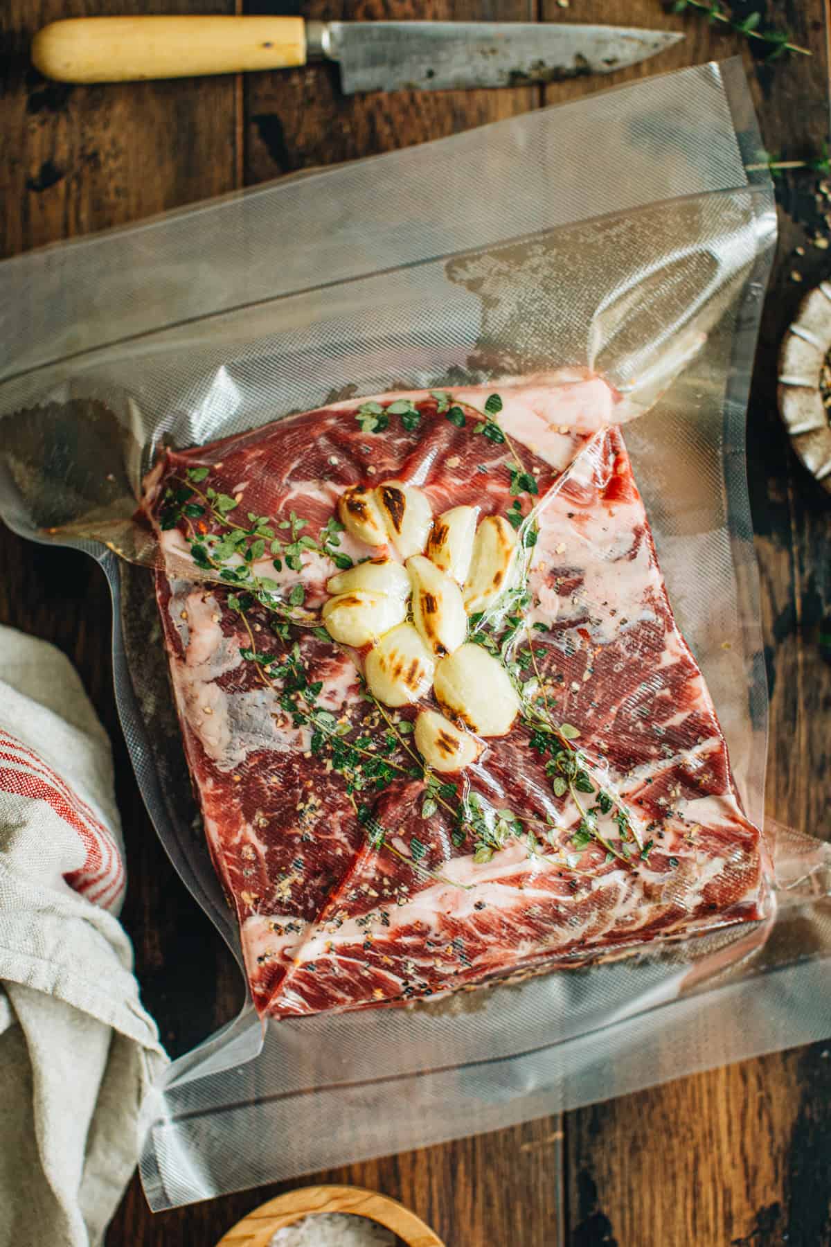 Prime rib roast topped with fresh thyme and garlic cloves sealed in a vacuum seal bag ready for sous vide.