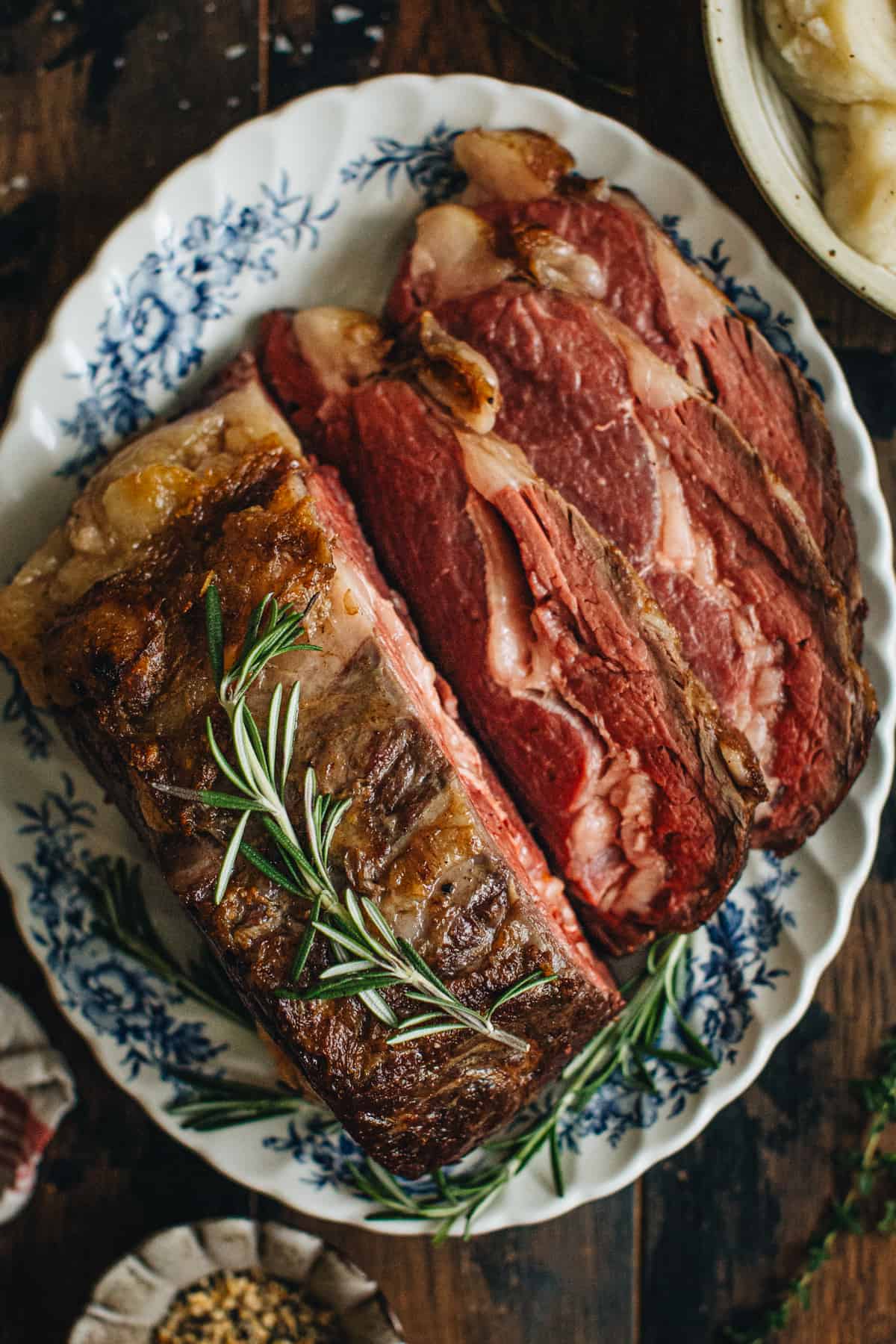 Sous vide prime rib topped with fresh rosemary and with 3 slices cut off laying beside it.