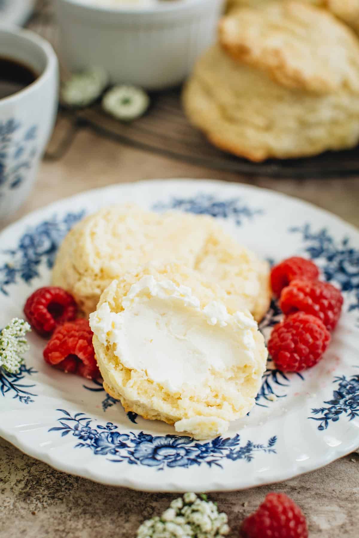 Sliced British scone covered in clotted cream on a plate with fresh raspberries.