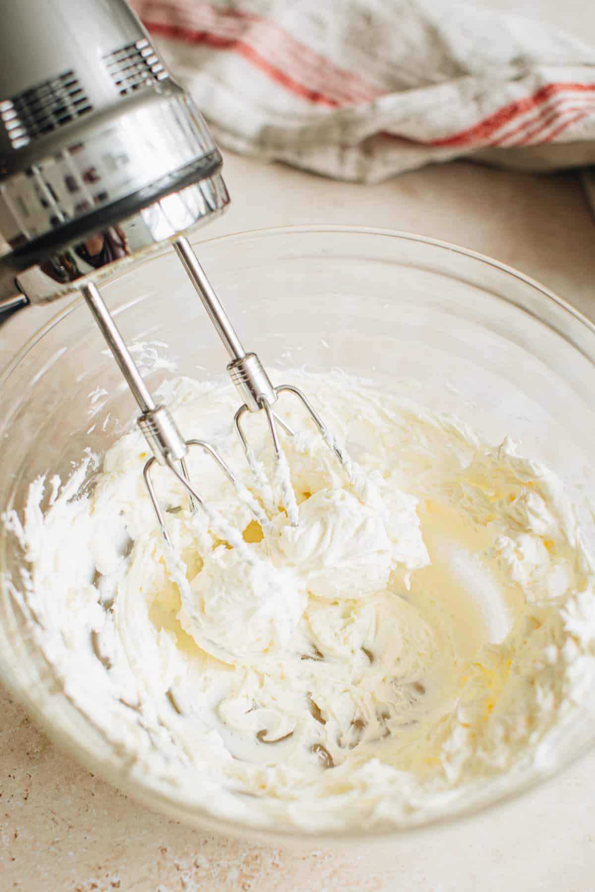 Beaten cream cheese in a mixing bowl for making crab dip with a handheld mixer sitting beside it.