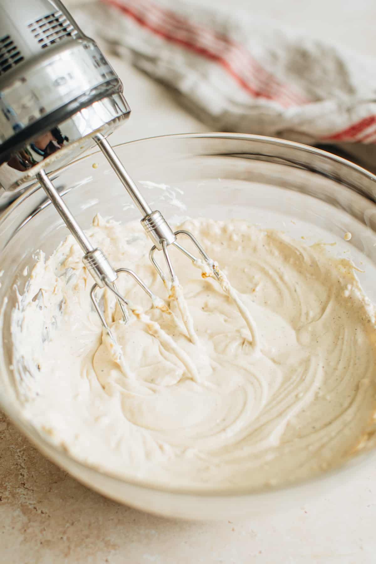 Crab dip base mixture in a mixing bowl with a handheld mixer beside it.