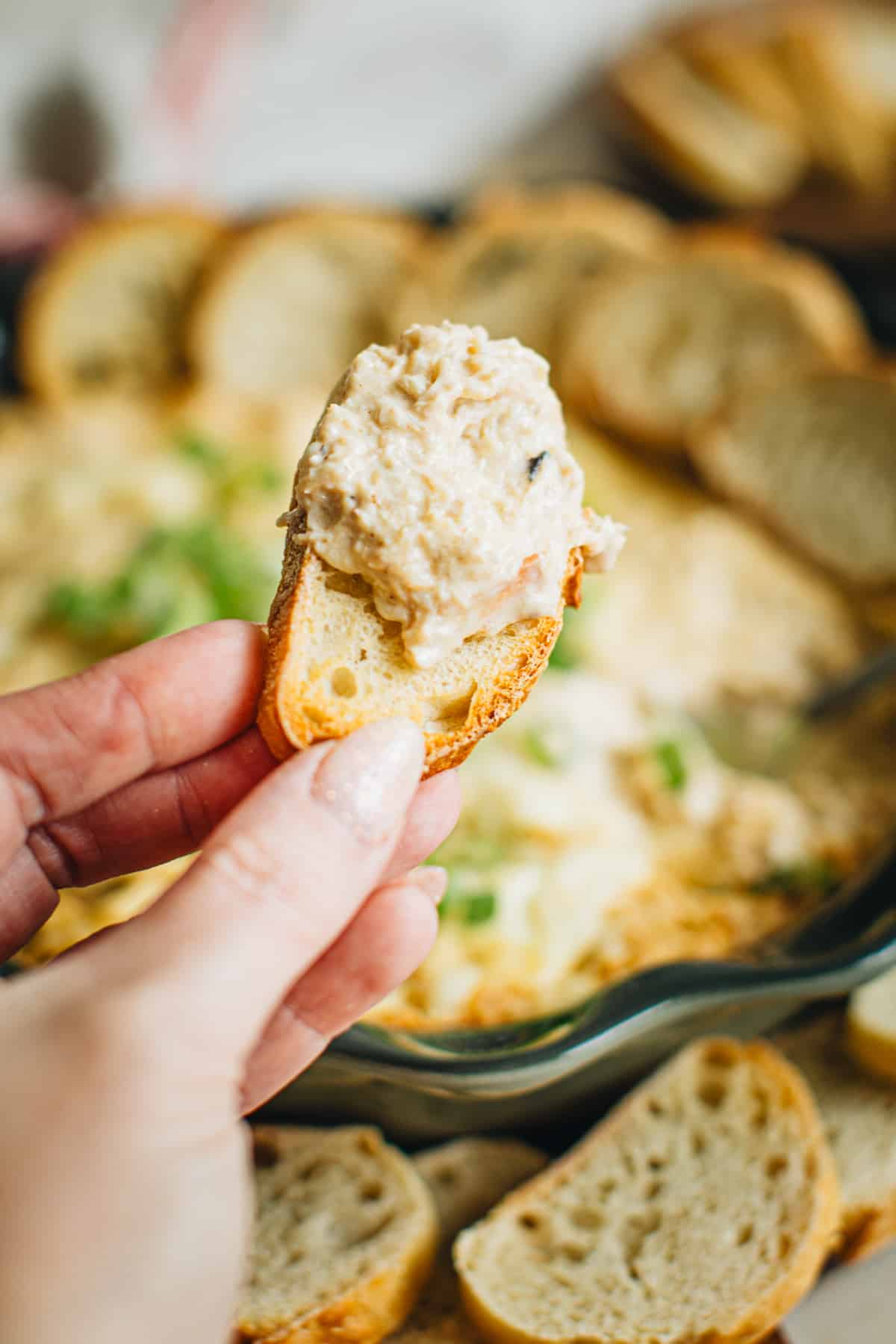 Hand holding a baguette slice covered in crab dip.