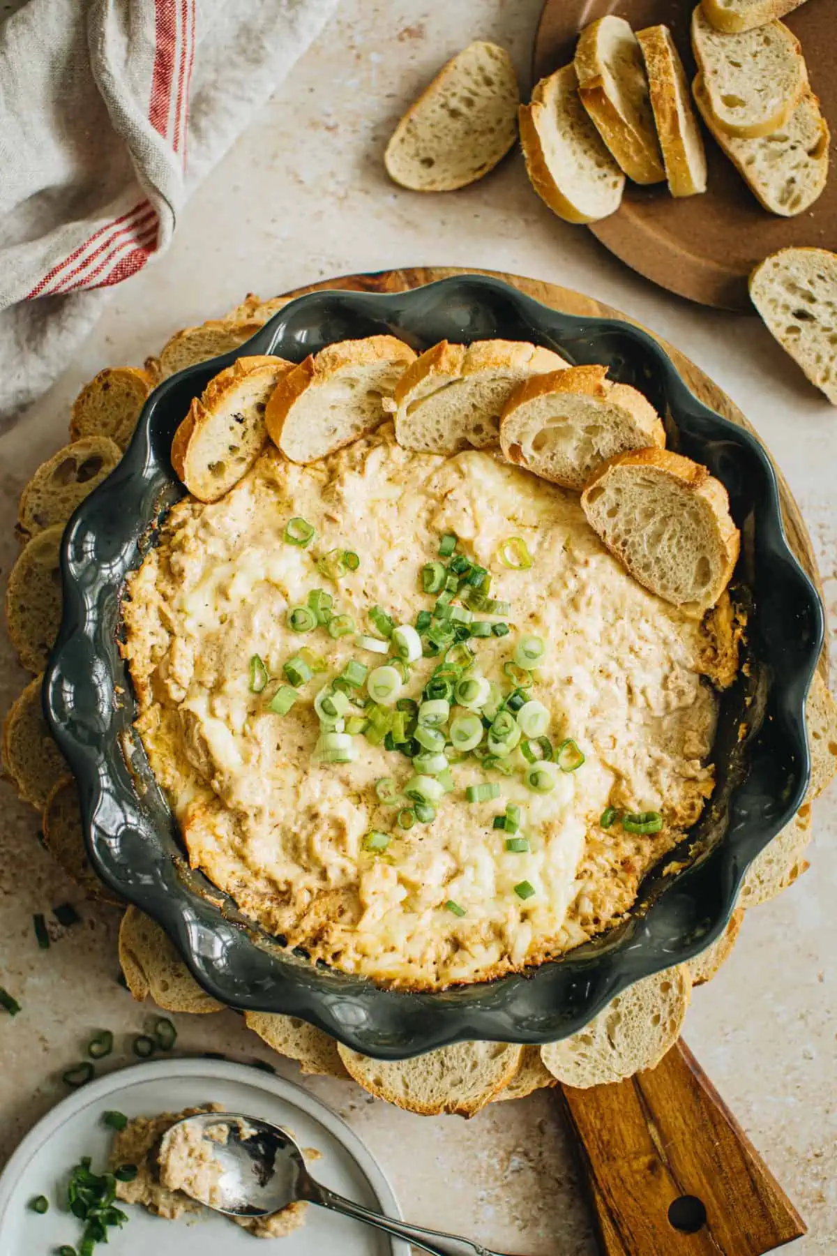Crab dip in a pie dish topped with green onions and surrounded by baguette pieces.