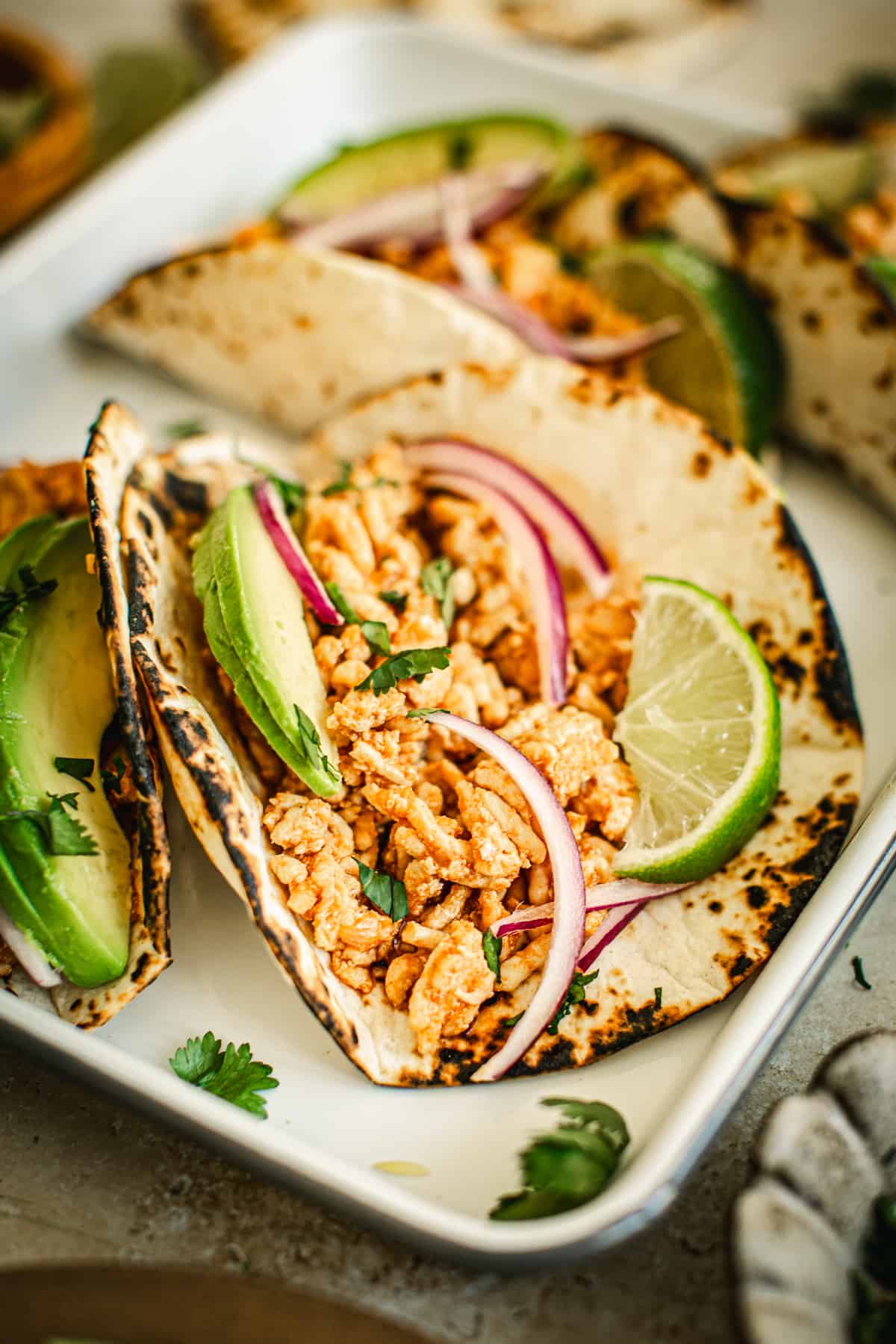 Ground chicken tacos on a tray topped with red onion, avocado, and limes.