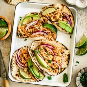 Ground chicken tacos on a tray topped with sliced onion and avocado.