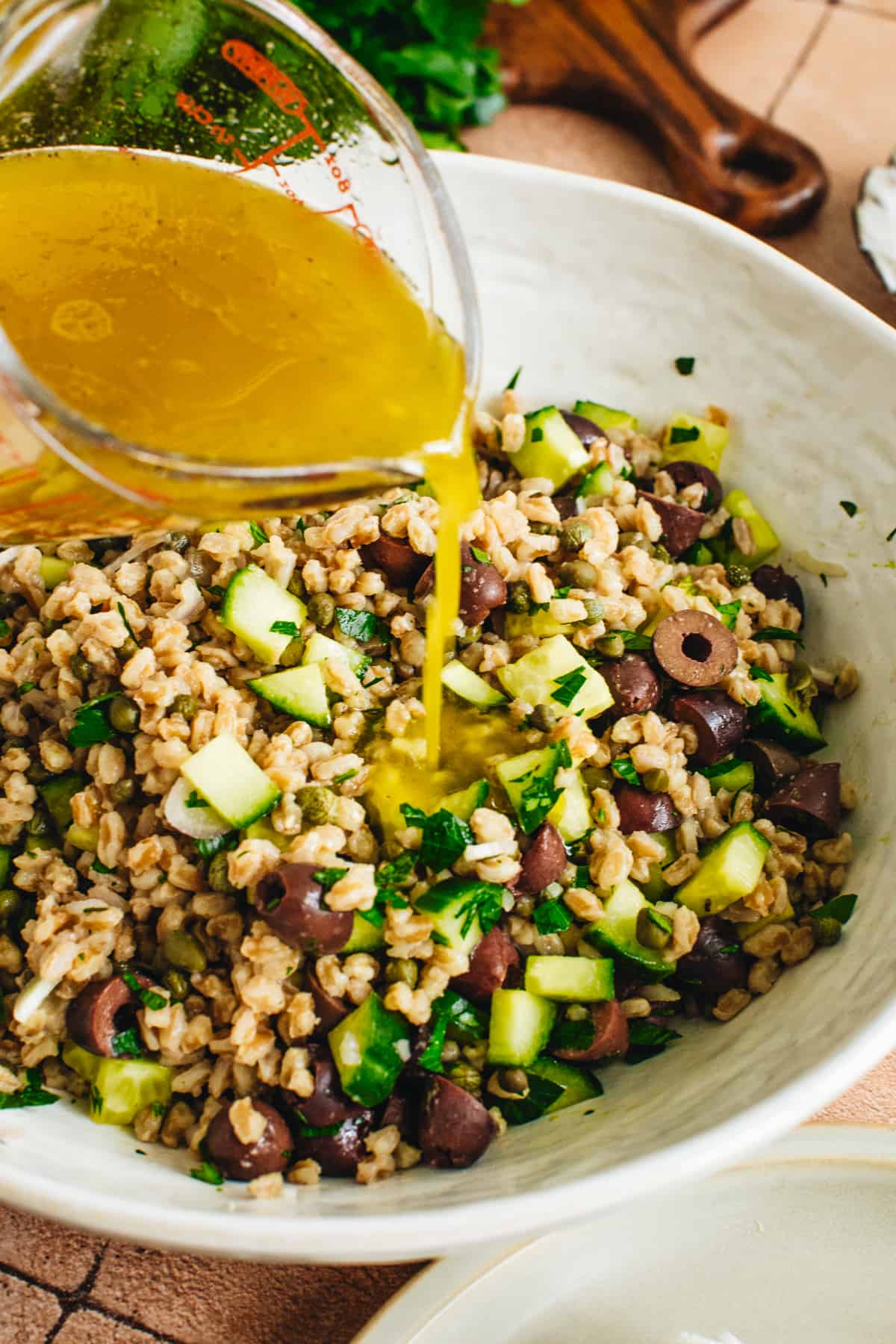 Pouring dressing over farro salad in a white mixing bowl.