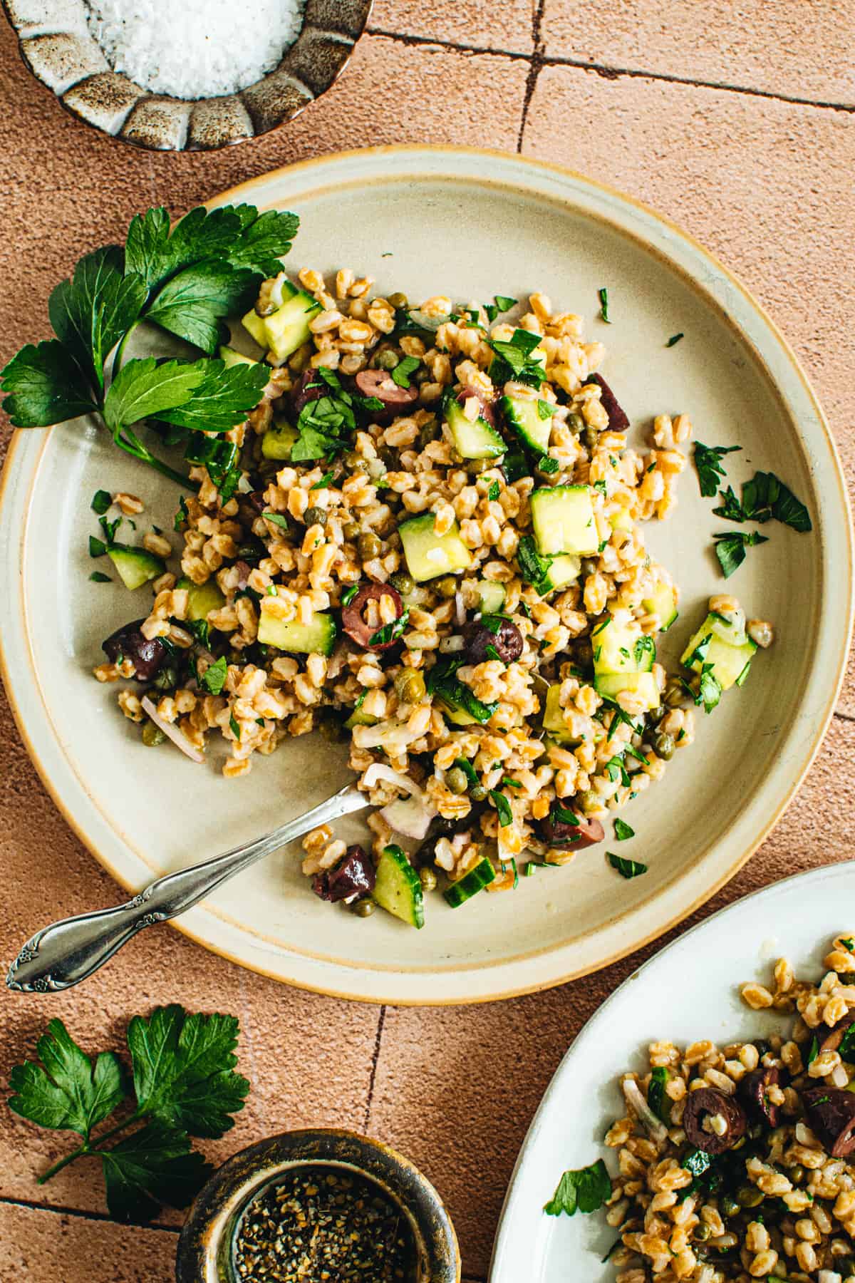 A fresh Farro Salad on a beige dinner plate garnished with parsley and with a silver spoon scooped into the salad.